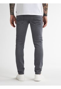 Vaqueros de mezclilla gris con un ajuste ceñido, bolsillos traseros con detalles de costura y zapatillas blancas desgastadas. La tela parece tener una textura ligeramente marcada.