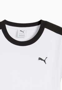 Biała koszulka z czarnym kołnierzykiem i akcentami na ramionach. Posiada małe czarne logo Puma na klatce piersiowej. Wykonana z miękkiego materiału.