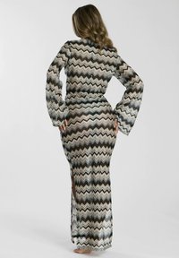 Vestido largo transparente con patrón de zigzag en beige, negro y crema, con mangas largas y slit laterales para mayor libertad de movimiento.