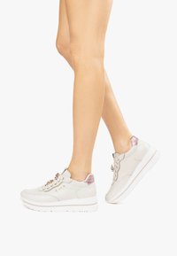 Sneakers beige chiaro con finitura in pelle liscia, dettagli metallici, accenti rosa sul tallone e una suola bianca spessa.