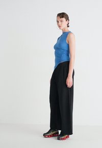 Top bleu fără mâneci cu pliere, pantaloni negri largi și pantofi sport negri și roșii. Design simplu și textură de țesătură netedă.