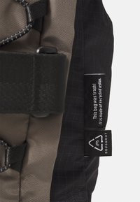 Siva i crna ruksak izrađena od recikliranog najlona, s mrežastom teksturom, gornjom ručkom i etiketom koja navodi da je od ekološki prihvatljivog materijala.