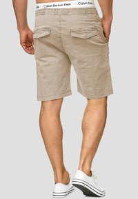 Beige puuvillashortsit suoran leikkauksen, joissa on kaksi takataskua, Calvin Kleinin vyötärö ja polvenpituinen muotoilu.