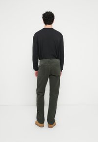 Pantalon en velours côtelé vert avec une coupe droite, des poches arrière et une finition texturée, associé à une chemise noire à manches longues.