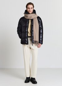 Giacca puffer nera lucida con cappuccio, sciarpa beige, maglione crema e pantaloni chiari. Stivaletti neri alla caviglia completano l'outfit.