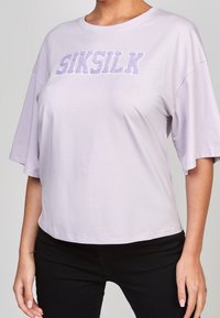 Ljuslila t-shirt med korta ärmar och lös passform, rundad halsringning, med texturerad "SIKSILK"-text i mörkare lila.