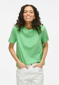 En mintgrøn kortærmet t-shirt med rund hals, glat tekstur, afslappet pasform, båret med hvide bukser, hænderne i lommerne.