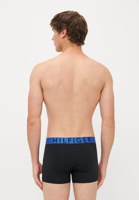 Schwarze Boxerbriefs mit einem blauen Gummibund, auf dem "HILFIGER" in Schwarz steht. Das Material wirkt glatt und hat eine enganliegende Passform.