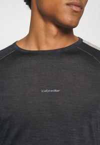 Svart kortärmad skjorta i mjukt tyg, med rund halsringning och en liten vit "icebreaker"-logotyp på bröstet. Texturerade ärmar.