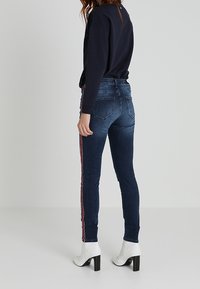 Smal jeans i mörkblå denim med röda och vita sidostrimmor. Har en mid-rise midja och diskreta bakfickor. Matchas med vita klackade ankelstövlar.