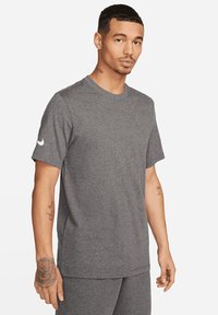 T-shirt grigia a maniche corte in tessuto morbido con scollo rotondo e un accento di logo bianco sulla manica sinistra, caratterizzata da una vestibilità comoda e una texture liscia.