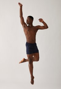 Shorts de bain bleu marine avec une taille élastique, en tissu léger et coupe décontractée, modèle en pose de saut avec les bras écartés.