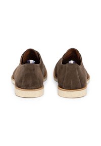 Zapatos de ante marrón con un perfil bajo, textura suave y una suela de goma de color claro. Cuentan con una lengüeta de tela en la parte posterior.