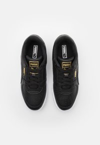 Black sneakers made of textured leather with gold accents, featuring a perforated design, white sole, and black laces.