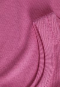 Rosa ribbad tyg som visar textur och lager, med slät och upphöjd ribbning. Materialet verkar mjukt och flexibelt.