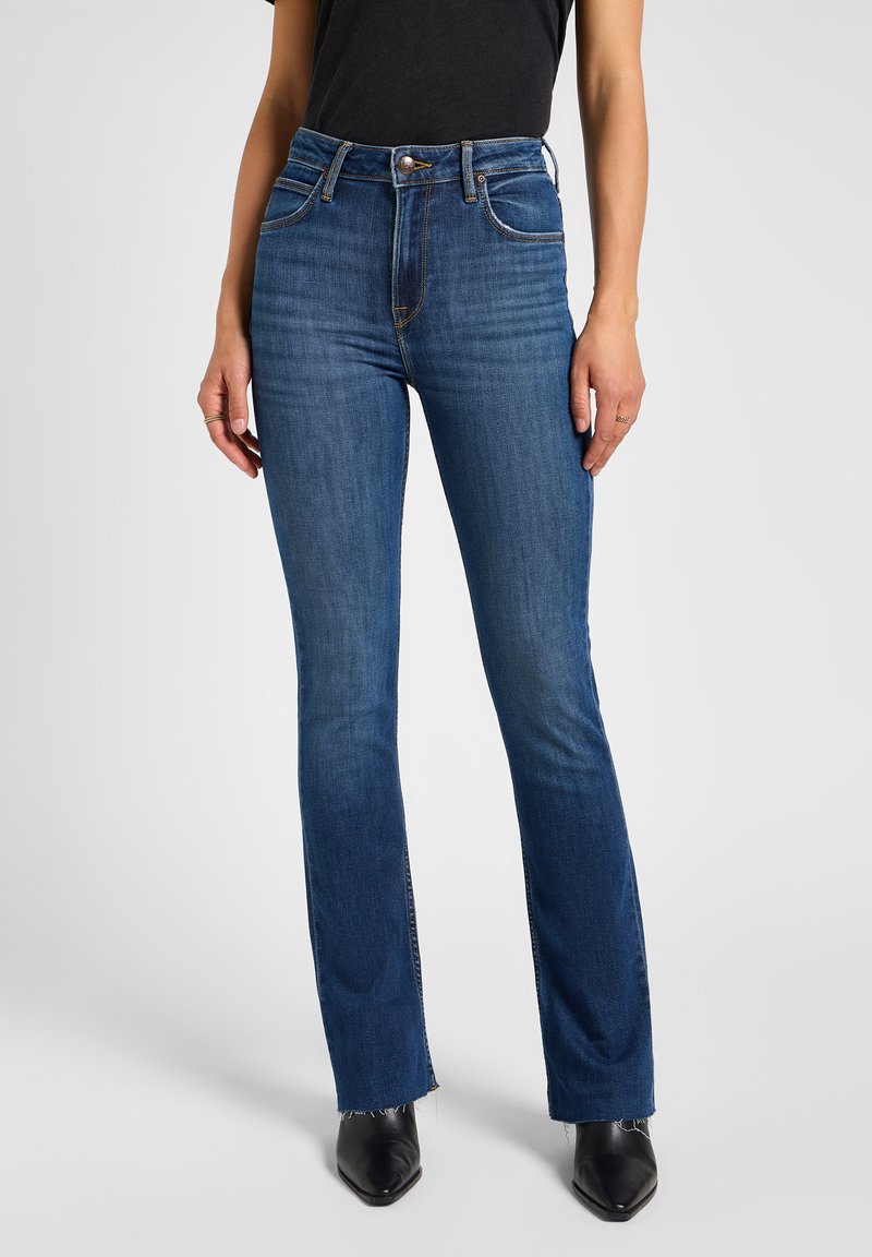 Jeans oscuros de tiro alto y pierna acampanada con un ligero desvanecimiento, dos bolsillos frontales y un diseño clásico de cinco bolsillos. El dobladillo presenta bordes sin terminar.