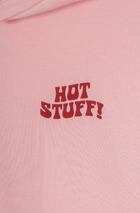 Tessuto di cotone rosa chiaro con del testo rosso audace che dice "HOT STUFF!" in un font giocoso e curvo. Texture liscia senza ulteriori dettagli.