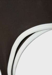 Gros plan sur un tissu noir avec un bord élastique blanc, montrant les coutures détaillées et la texture.