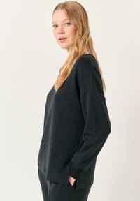 Felpa nera realizzata in materiale morbido, con vestibilità rilassata, maniche lunghe e tasche laterali, bordi a costine e orlo leggermente curvo.