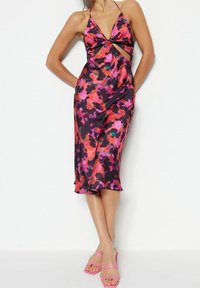 Satin midiklänning med ett svart, rosa och grönt blommönster, en knutdetalj vid bysten och urtagna sidor. Kombinerat med rosa sandaler med remmar.