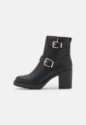 Zwarte enkellaarsjes van nepleer, met twee gouden gespen, een chunky hak en een gestructureerde zool voor grip.