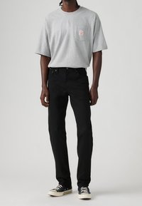 Camiseta gris de manga corta con un bolsillo en el pecho; combinada con jeans negros y zapatillas bajas negras con cordones blancos.