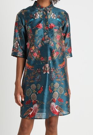 Sininen satiinimekko, jossa on kukka- ja lintukirjailu, puolihihat ja kauluksellinen pääntie, päällä tummaihoinen henkilö.