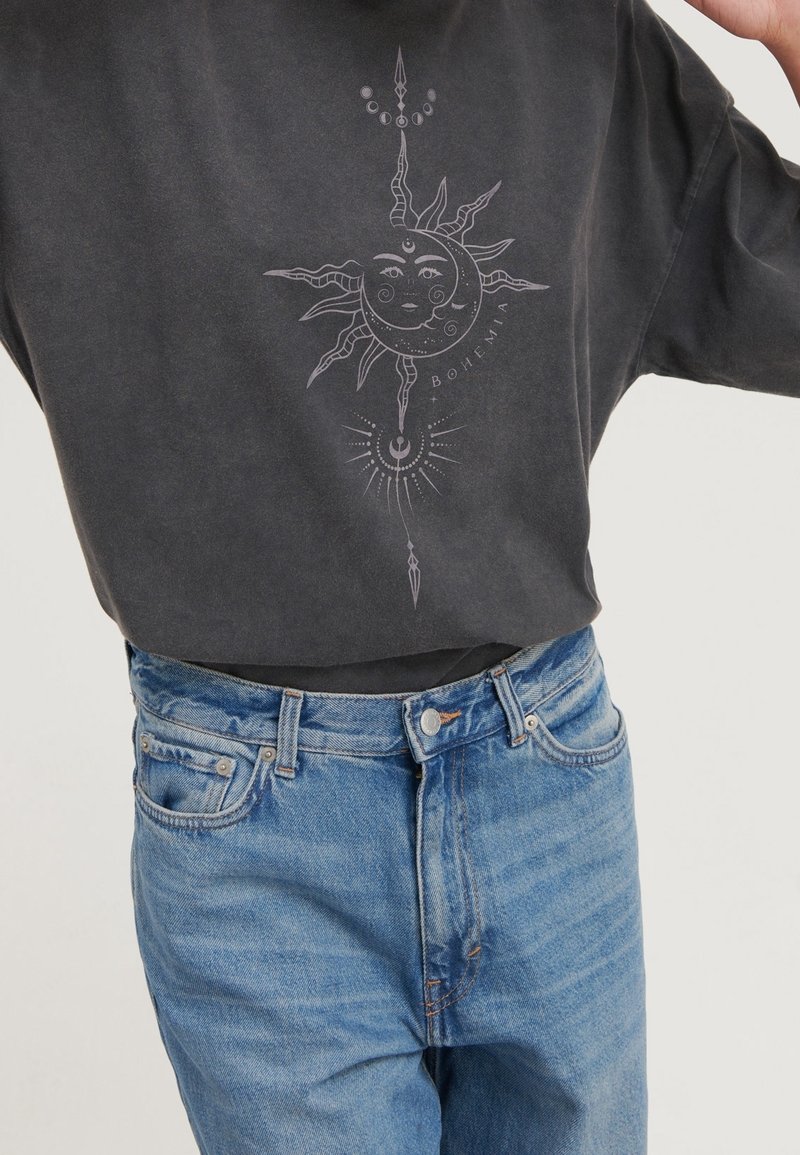 Černé oversize tričko s grafikou slunce a měsíce ve světle šedé barvě. Kombinované s džíny s vysokým pasem v modré barvě.