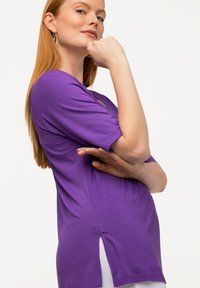 T-shirt viola realizzata in morbido cotone, con maniche corte, scollatura a barca e spacco laterale per facilitare i movimenti.