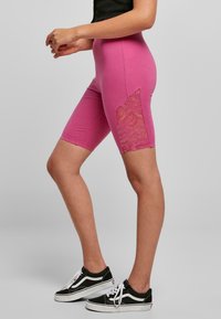 Pantalones cortos de bicicleta rosas hechos de algodón suave, con un panel de encaje a los lados. El diseño es ajustado y llega hasta la rodilla.