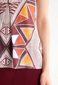 Top senza maniche con una stampa geometrica multicolore in tonalità terrose, con arancione, blu e dettagli di linee, realizzato in tessuto leggero.