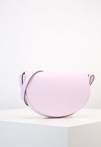 Kulatá kabelka z jemné růžové kůže s hladkým povrchem. Disponuje černým popruhem a minimalistickým designem. Na přední straně se nachází výrazné embosované logo.
