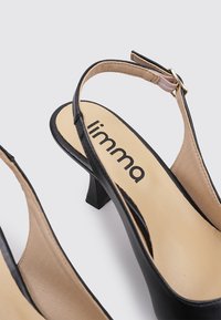 Zapatos de tacón abiertos negros con un bajo tacón en bloque, que cuentan con una correa al tobillo en tono nude y un forro interior suave. Nombre de la marca "limma" visible.