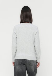 Lichtgrijze trui met lange mouwen, ronde halslijn en geribde zoom. Zachte textuur met subtiele stiksels aan de achterkant. Gecombineerd met donkergrijze jeans.