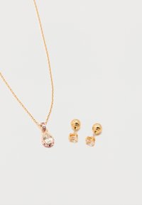 Χρυσό κολιέ με κρεμαστό κρύσταλλο σε σχήμα σταγόνας και ζευγάρι χρυσά καρφωτά σκουλαρίκια με διαυγή τετράγωνα κρύσταλλα σε λευκό φόντο.