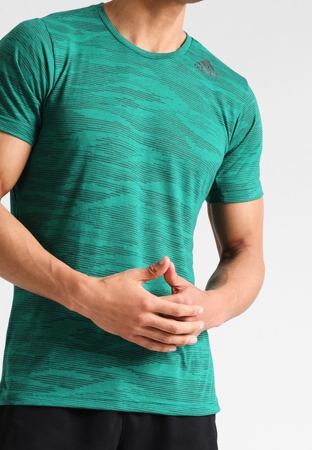 Zelené sportovní tričko s texturovaným vlnitým vzorem, kulatým výstřihem a krátkými rukávy; nahoře vlevo na hrudi je logo Adidas.