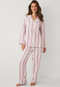 Ensemble de pyjama rayé aux couleurs rose pâle et blanc. Haut boutonné à manches longues avec pantalon assorti à jambes larges. Tissu léger.
