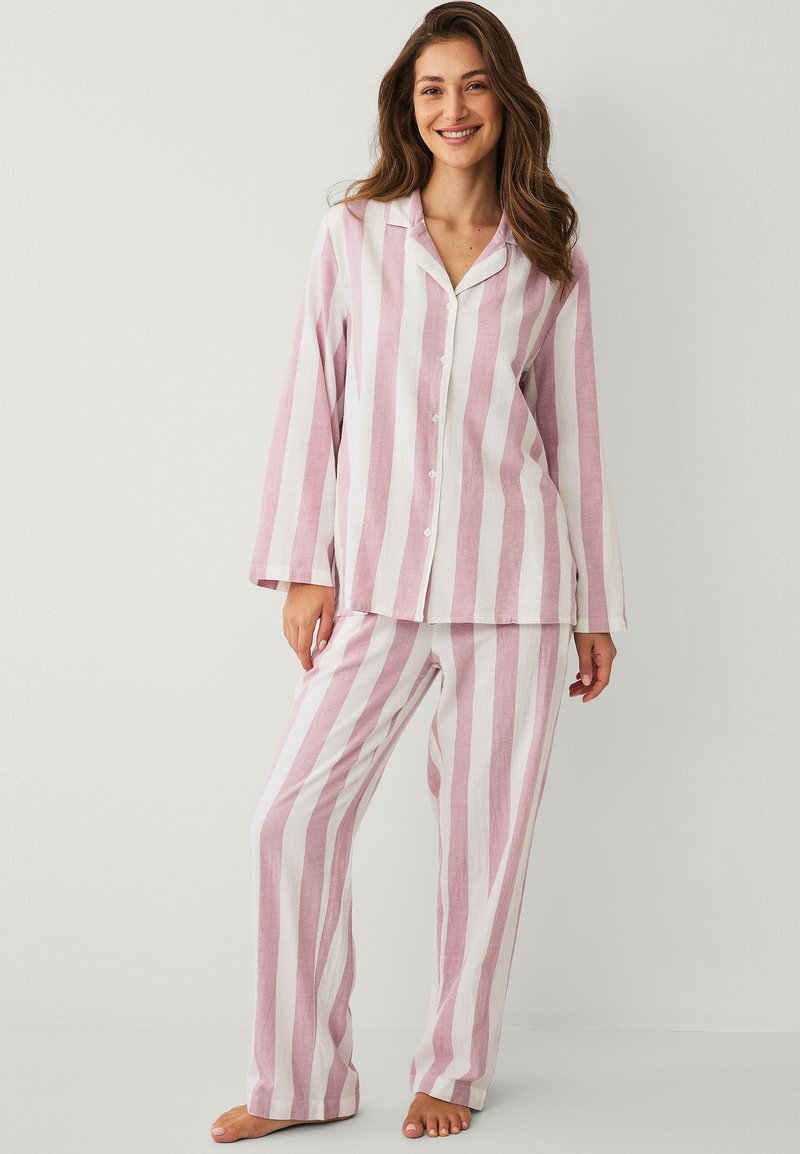 Ensemble de pyjama rayé aux couleurs rose pâle et blanc. Haut boutonné à manches longues avec pantalon assorti à jambes larges. Tissu léger.