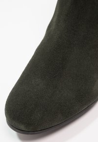 Botte de cheville en daim vert foncé avec un bout arrondi et une texture lisse, dotée d'un léger éclat et d'un design épuré et minimaliste.