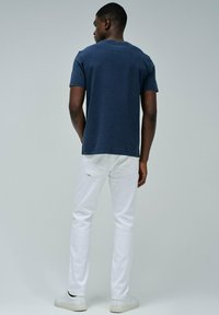 Camiseta de algodón azul marino con cuello redondo, combinada con jeans de mezclilla blancos y zapatillas blancas. Vista desde la parte de atrás que resalta el diseño.