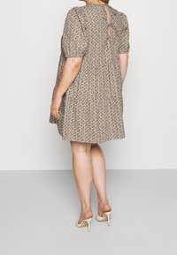 Kwiatowa sukienka z krótkimi bufkami, beżowa tkanina z małymi brązowymi i zielonymi kwiatami, z tyłu kluczowy otwór, w połączeniu z cielistymi sandałami na obcasie.