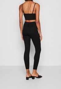 Top corto ajustado negro y leggings de cintura alta, hechos de una tela suave. Presenta tirantes delgados y un diseño elegante. Combinado con tacones negros de deslizar.