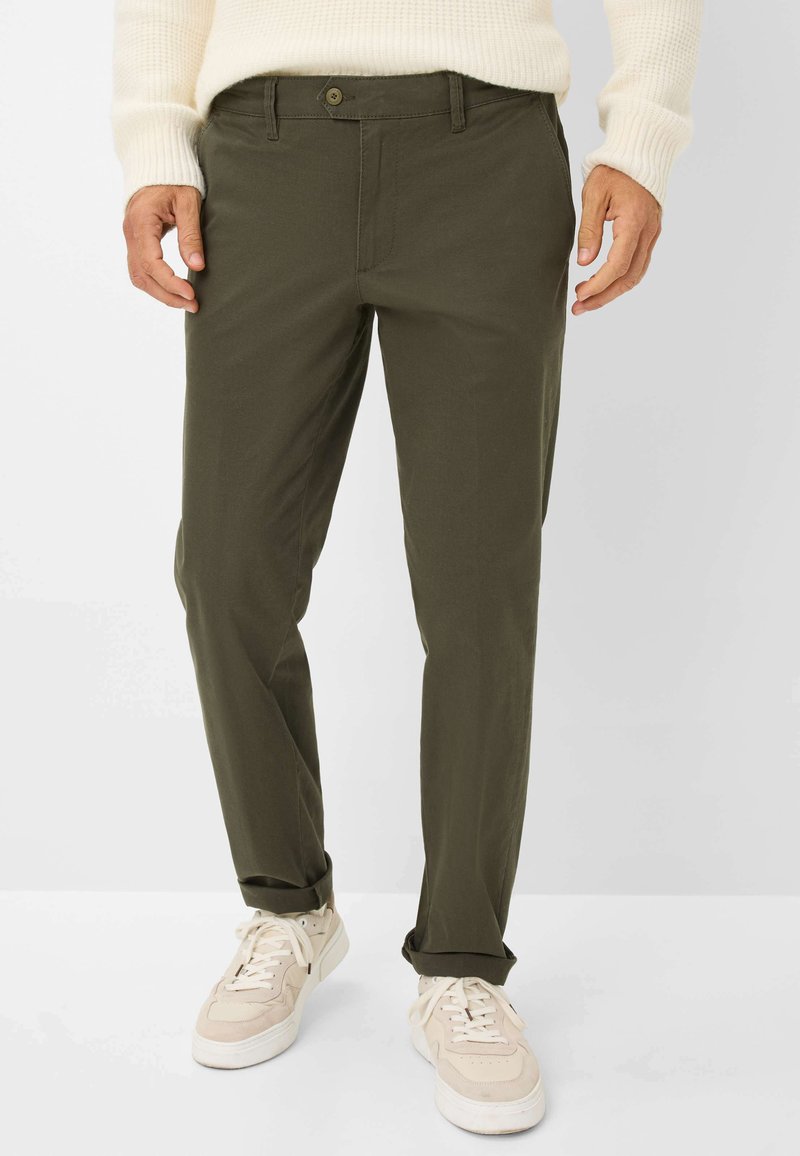 Oliven grønne bukser lavet af en bomuldsblanding, med et lige ben design og frontlommer, parret med cremefarvede sneakers.