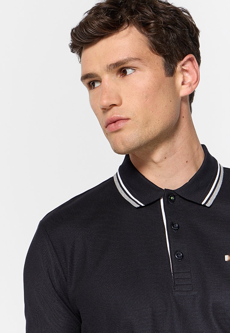 Schwarzes Poloshirt mit strukturierter Oberfläche, ausgestattet mit einer Knopfleiste mit drei Knöpfen, einem gestreiften Kragen in Weiß und Grau sowie einem kleinen Logo auf der Brust.