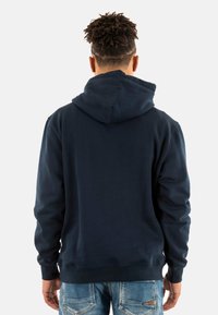 Marineblauwe hoodie met een koord in de capuchon, zachte textuur en geribde manchetten, gecombineerd met lichtblauwe distressed jeans.