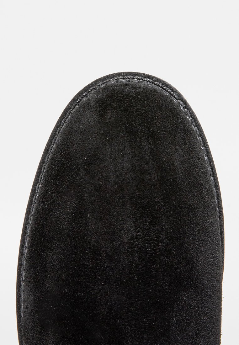 Schwarzer Wildlederschuh zum Reinrutschen mit runder Zehenpartie, strukturiertem Obermaterial und kontrastierenden Nähten entlang der Kante. Schlichtes Design für einfaches Tragen.