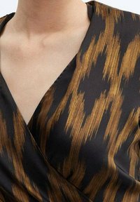 Top noir enveloppant avec un motif texturé de rayures verticales marron doré. Fabriqué dans un tissu lisse avec un design en V.