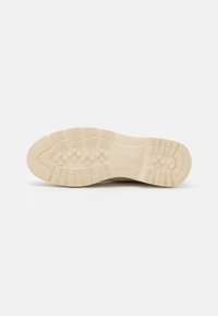 Semelle de sneaker beige en caoutchouc texturé, avec un motif de semelle pour une meilleure adhérence. Design sobre, sans accents ni logos notables.