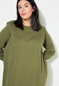 Vestido sudadera en verde oliva, de mangas largas, corte relajado, textura de canalé, tela suave, con detalles en los hombros, diseño minimalista.