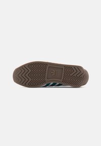 Brun Adidas skosula med zigzag-mönster och centralt fyrkantigt märke med trefoil och "Adidas" text.